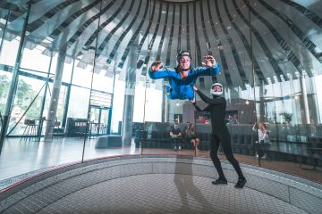Ein Mann fliegt und ein Mann steht im Windkanal In der Jochen Schweizer Arena