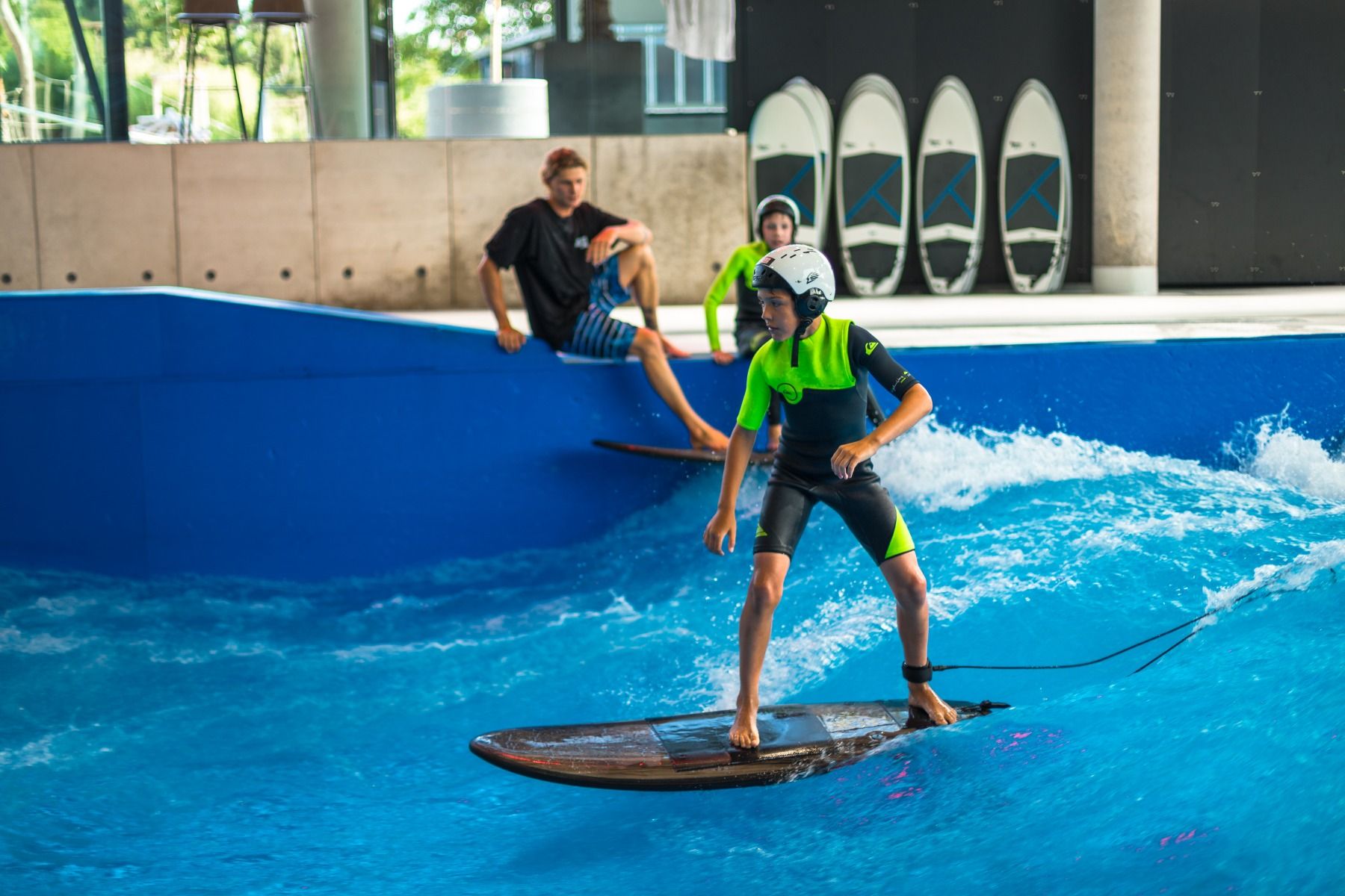 Bild - EIn Kind mit Helm surft auf der Indoorwelle in der Jochen Schweizer Arena