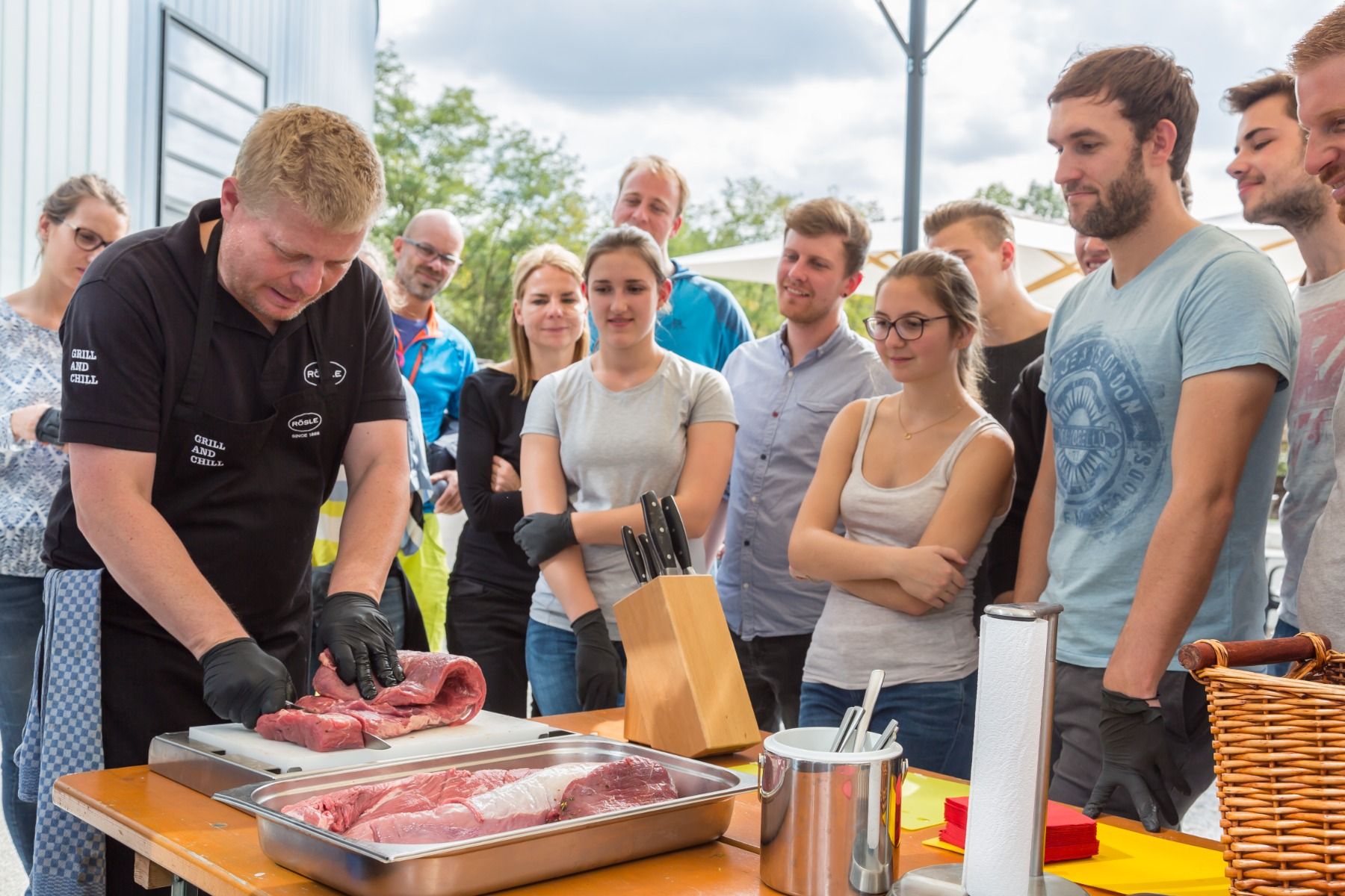 Bild - Ein Grillmeister zeigt einer Gruppe von Menschen wie man am besten Fleisch schneidet
